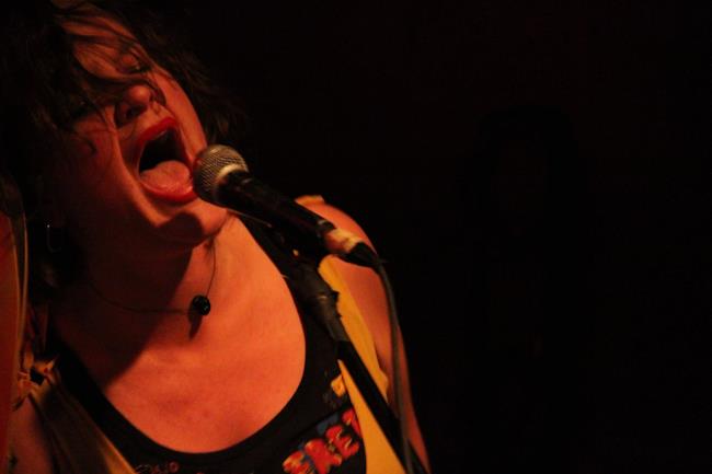 A woman singing into a microphone on a yellow-lit stage.